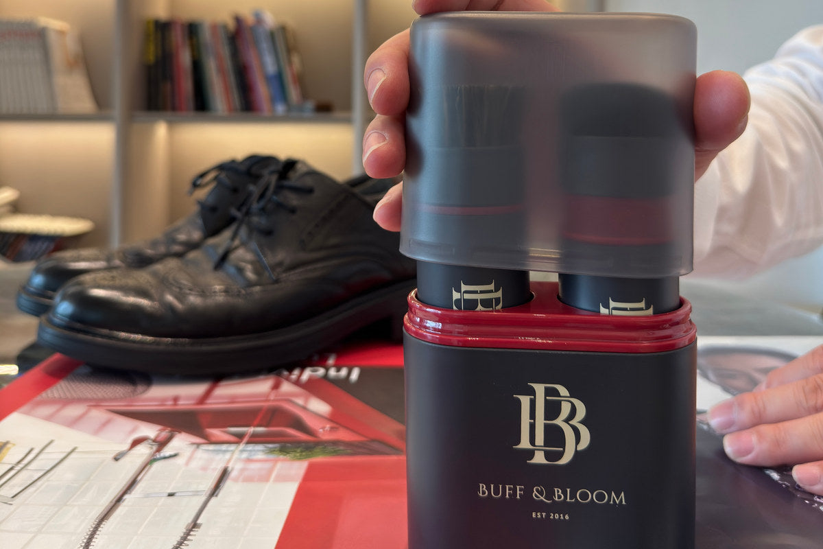 Hand holding the Buff & Bloom storage cover over the shoe polish kit beside black leather shoes