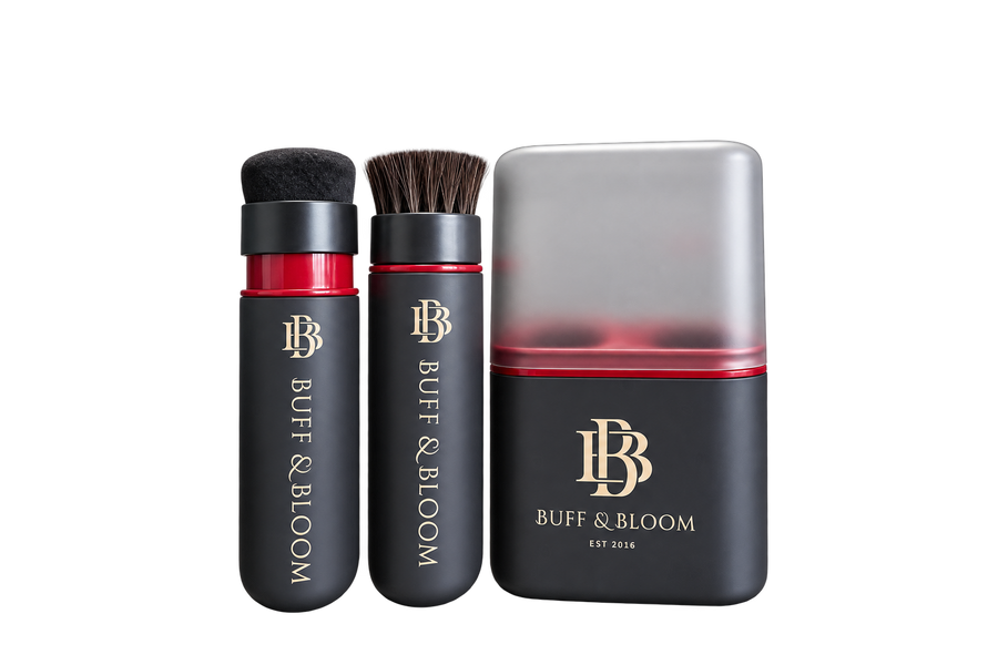Buff & Bloom makeup set featuring a black cylindrical brush with black bristles, a black cylindrical sponge applicator with brown bristles, and a matching rectangular sponge block with a translucent gray top and red gradient base, all on a white background.